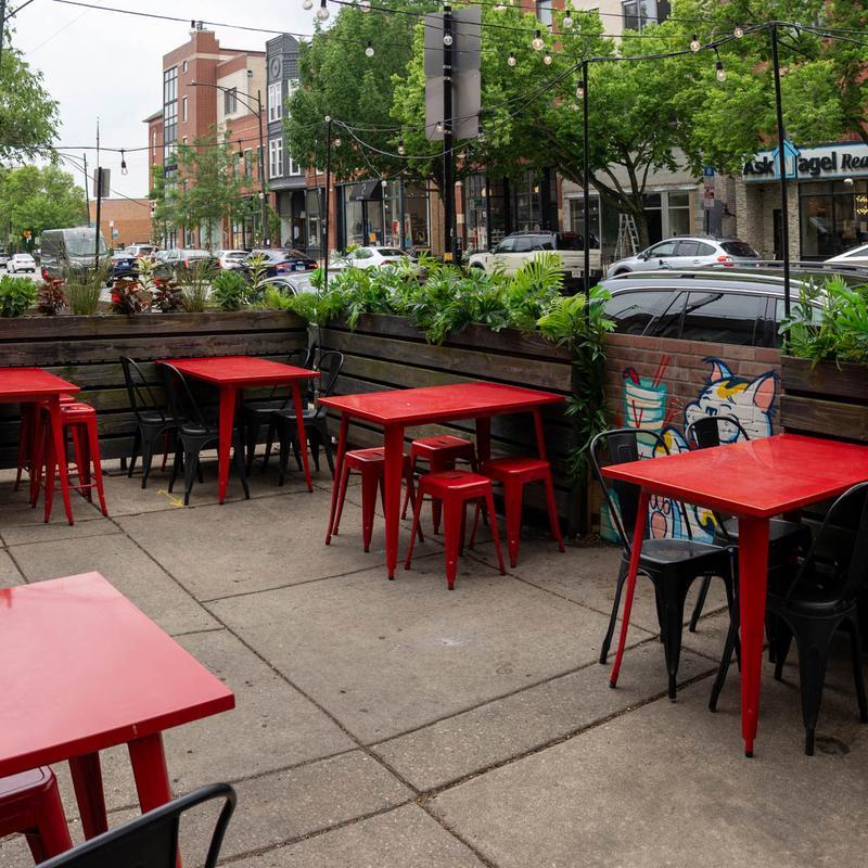 Outdoor restaurant patio with red metal tables, stools, and black chairs