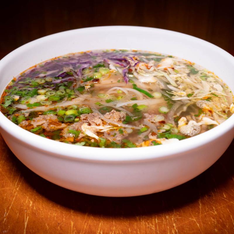 Bowl of Vietnamese beef pho with rice noodles, scallions, and herbs