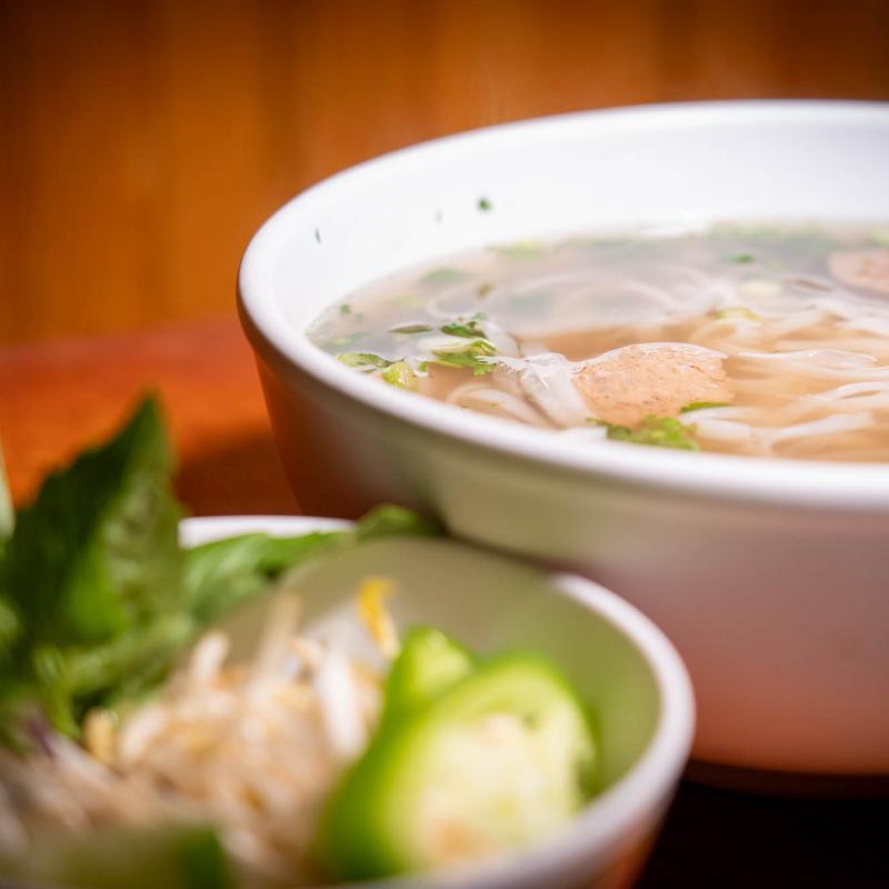 Bowl of chicken pho with rice noodles, meatballs, herbs and lime