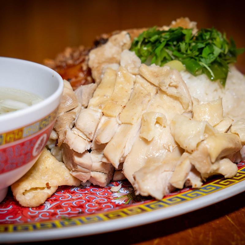 Hainanese chicken rice with poached chicken, rice, herbs, and clear soup