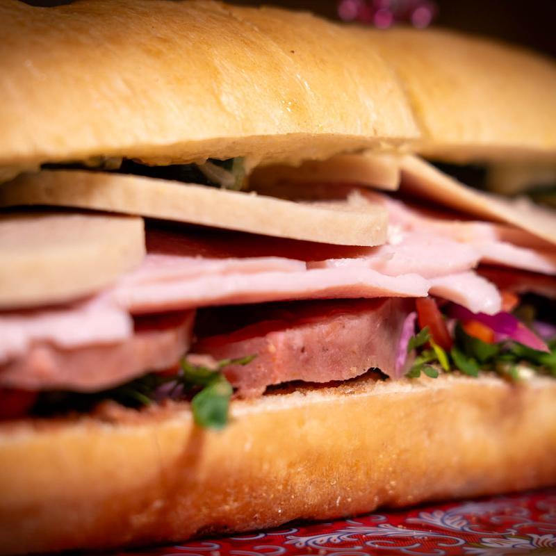 Deli sandwich with layered ham, bologna, cheese, and microgreens