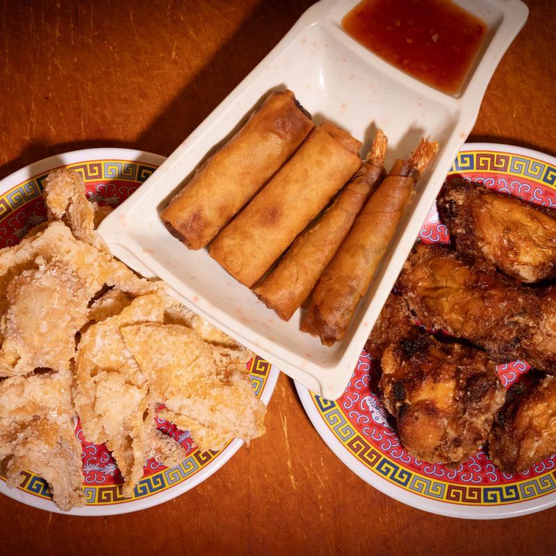 Plate of fried spring rolls with dipping sauce, crispy chicken wings and popcorn chicken