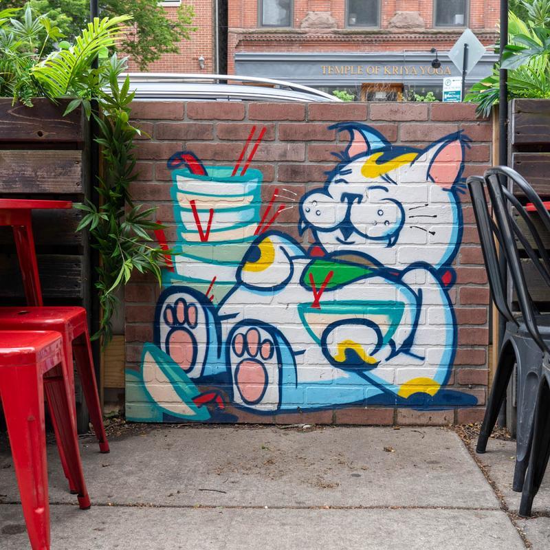 Mural of a relaxed maneki-neko cat holding bowls with chopsticks